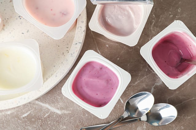 Composition with plastic cups with yogurt on grey table