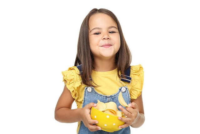 Beautiful little girl with potato chips in bowl on white background