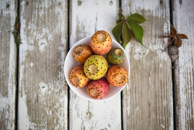 Colorful juicy prickly pear fruit on a white plate and a white wooden background. Edible cactus on the table, prickly pear apples