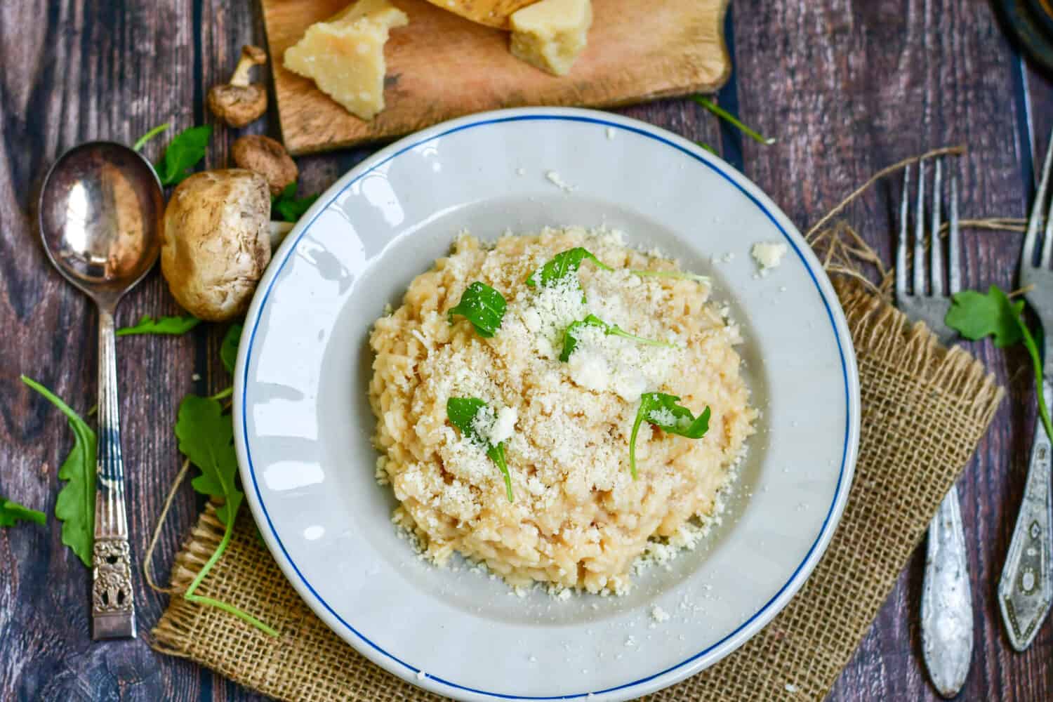 Italian creamy cheese risotto with parmesan cheese and fresh basil on rustic background