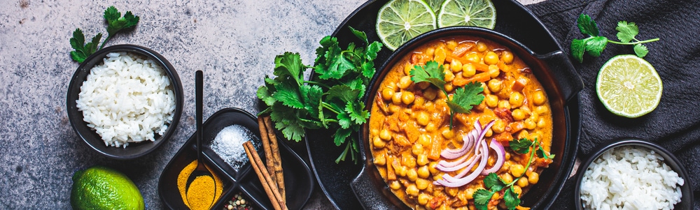 Vegan chickpea curry with rice and cilantro in a black bowl, dark background. Indian cuisine concept.