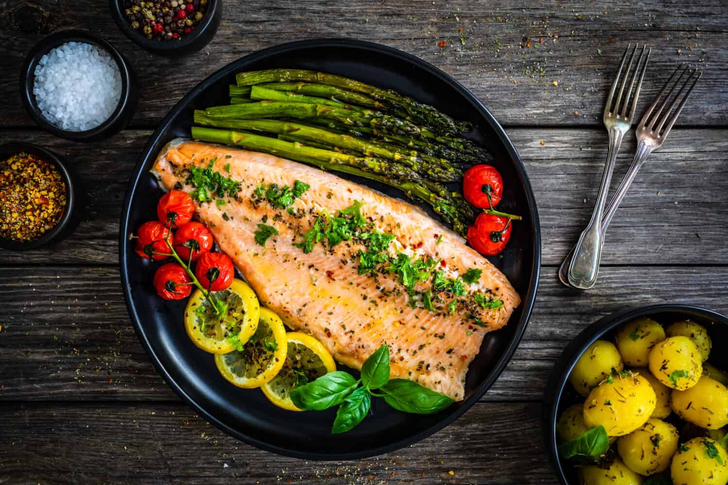 Roasted trout fillet with asparagus and vegetables served on black plate on wooden table