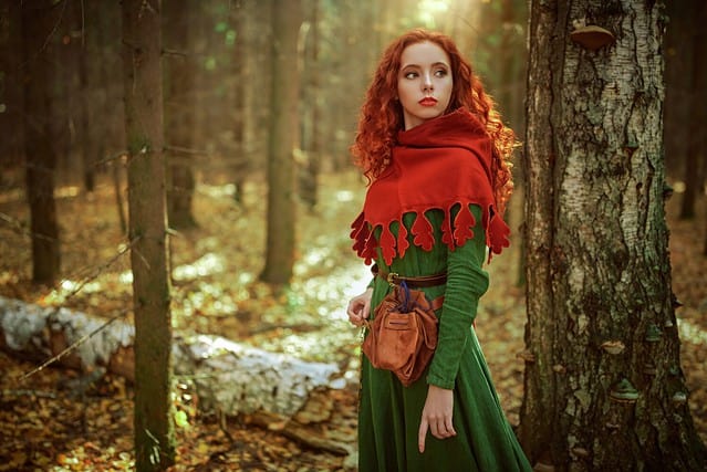Celtic culture. Fantasy world. Portrait of a beautiful red-haired girl of the Middle Ages standing in the dense forest.