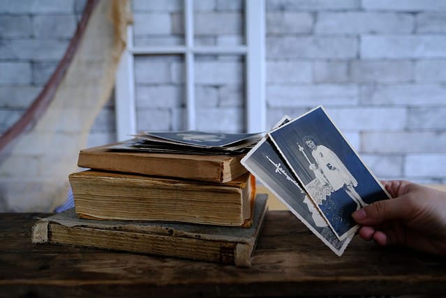 female hand holds vintage photos, retro photography of 1940-1950 on wooden table, old books, concept of genealogy, memory of ancestors, family tree, genealogy, childhood memories, family archive
