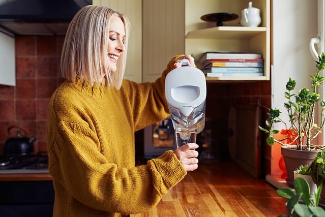 Smiling mature woman pouring filtered water into glass at kitchen