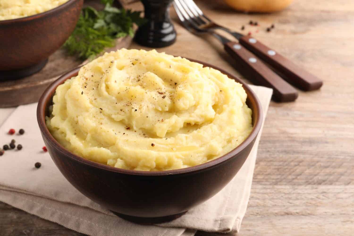 Bowl of tasty mashed potatoes with black pepper served on wooden table