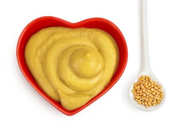 Mustard sauce in ceramic bowl with seed isolated on white background. Top view. Flat lay