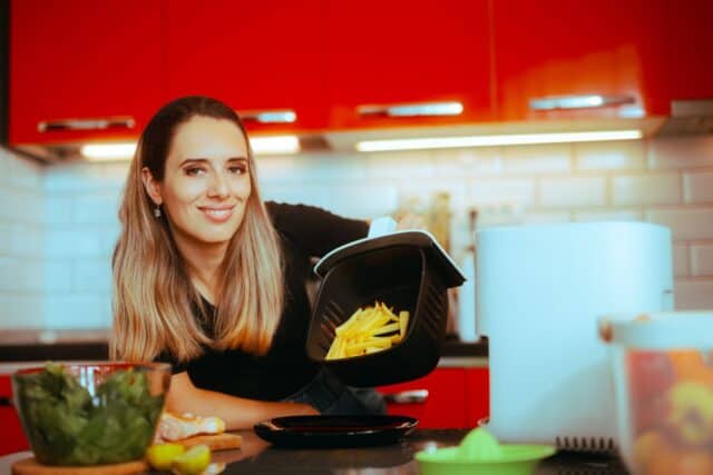 Happy Woman Cooking Healthy French Fries in an Air Fryer. Girl preparing at home a healthier version of a fast food dish