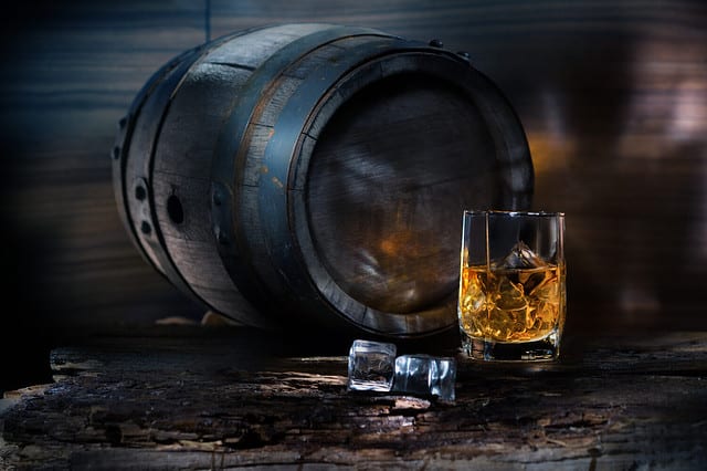 glass of whiskey with ice near the vintage barrels