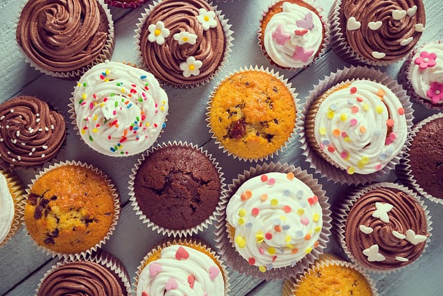 Multiple colorful nicely decorated muffins on a wooden background, top view