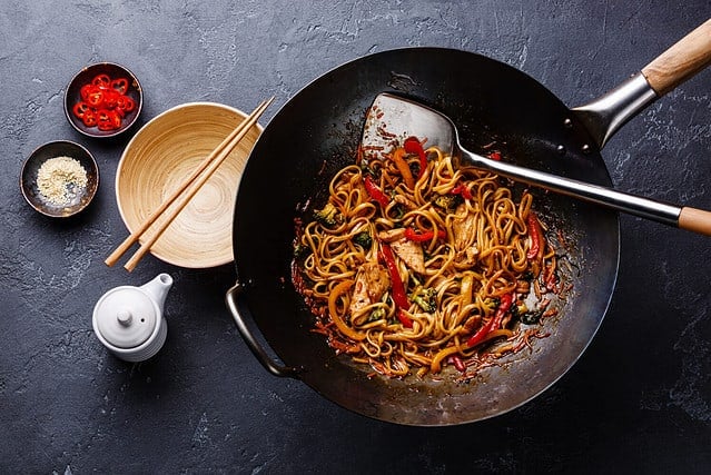 Pan fried noodles with chicken and vegetables in wok pan on dark stone background