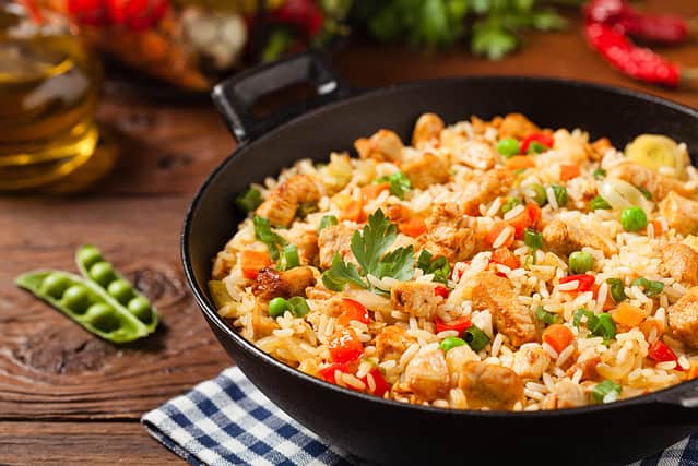 Fried rice with chicken. Prepared and served in a wok. Natural wood in the background. Front view.