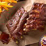 A rack of delicious baby back ribs with barbecue sauce, french fries, coleslaw and beer.