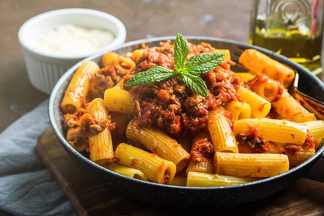 Delicious rigatoni pasta with Italian tomato meat ragu sauce served in a pan on dark brown background. Traditional pasta dish concept. Home made lunch