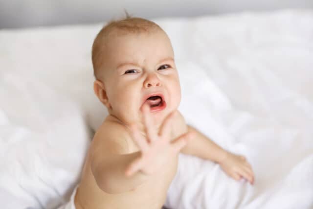 Cute nice little baby girl crying lying with her mom on bed at home.
